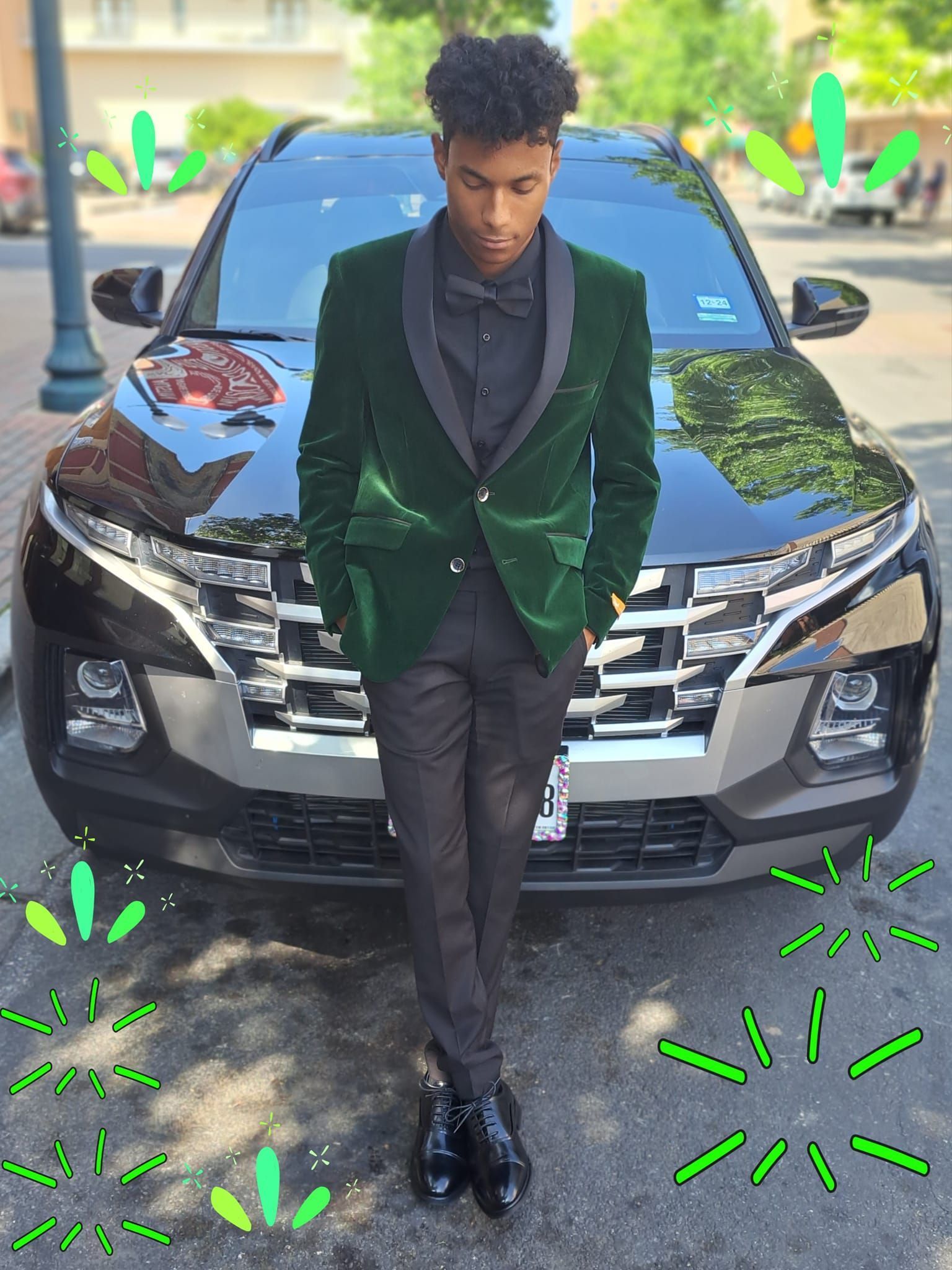 A man in a green suit is standing in front of a black car.