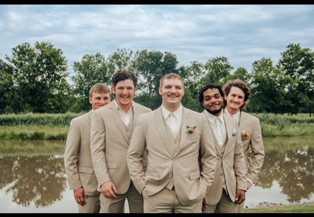 The groom and his groomsmen are posing for a picture in front of a lake.