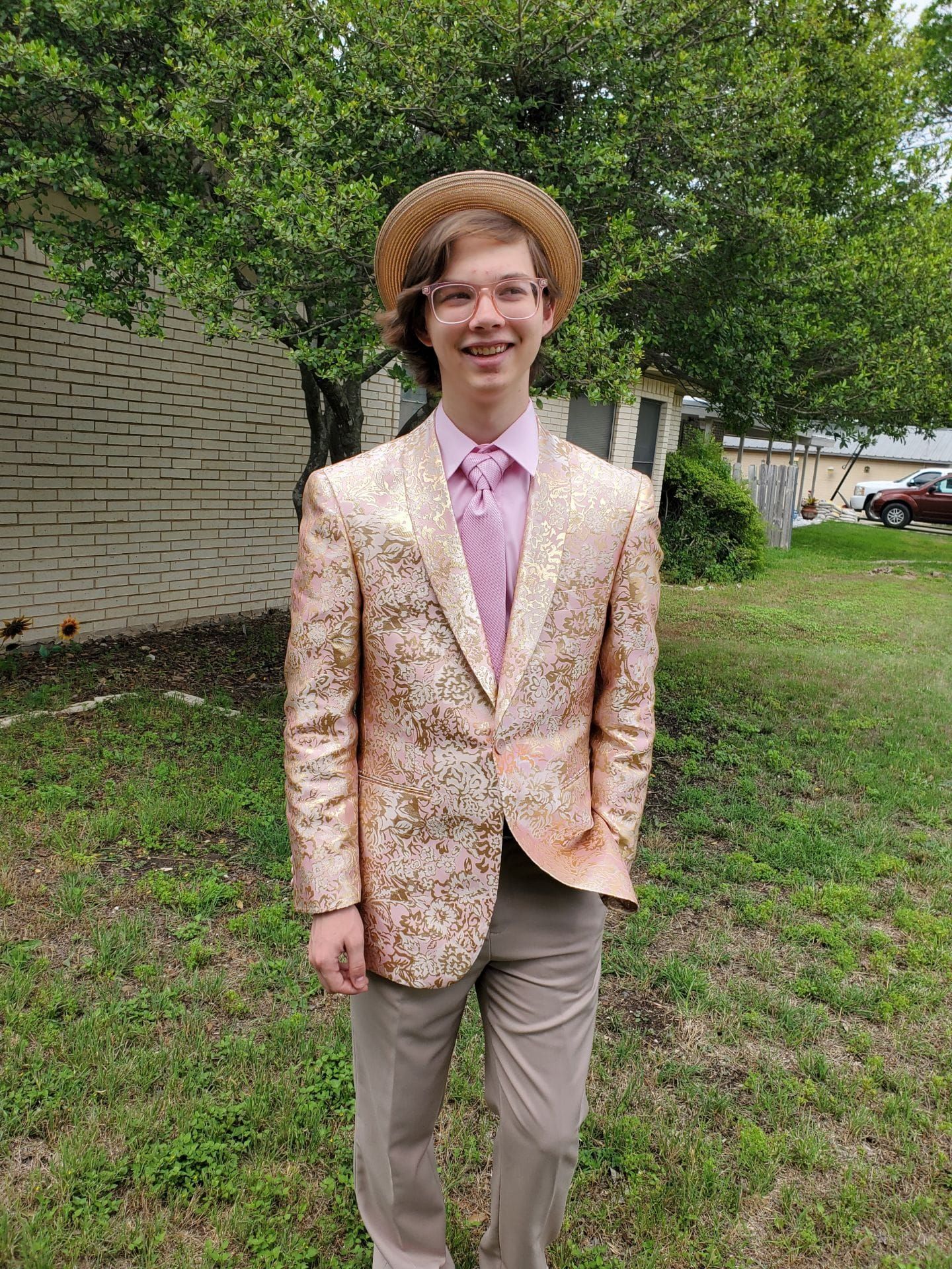 A young man in a suit and hat is standing in the grass.