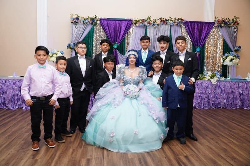 A woman in a ball gown is posing for a picture with a group of boys in suits.