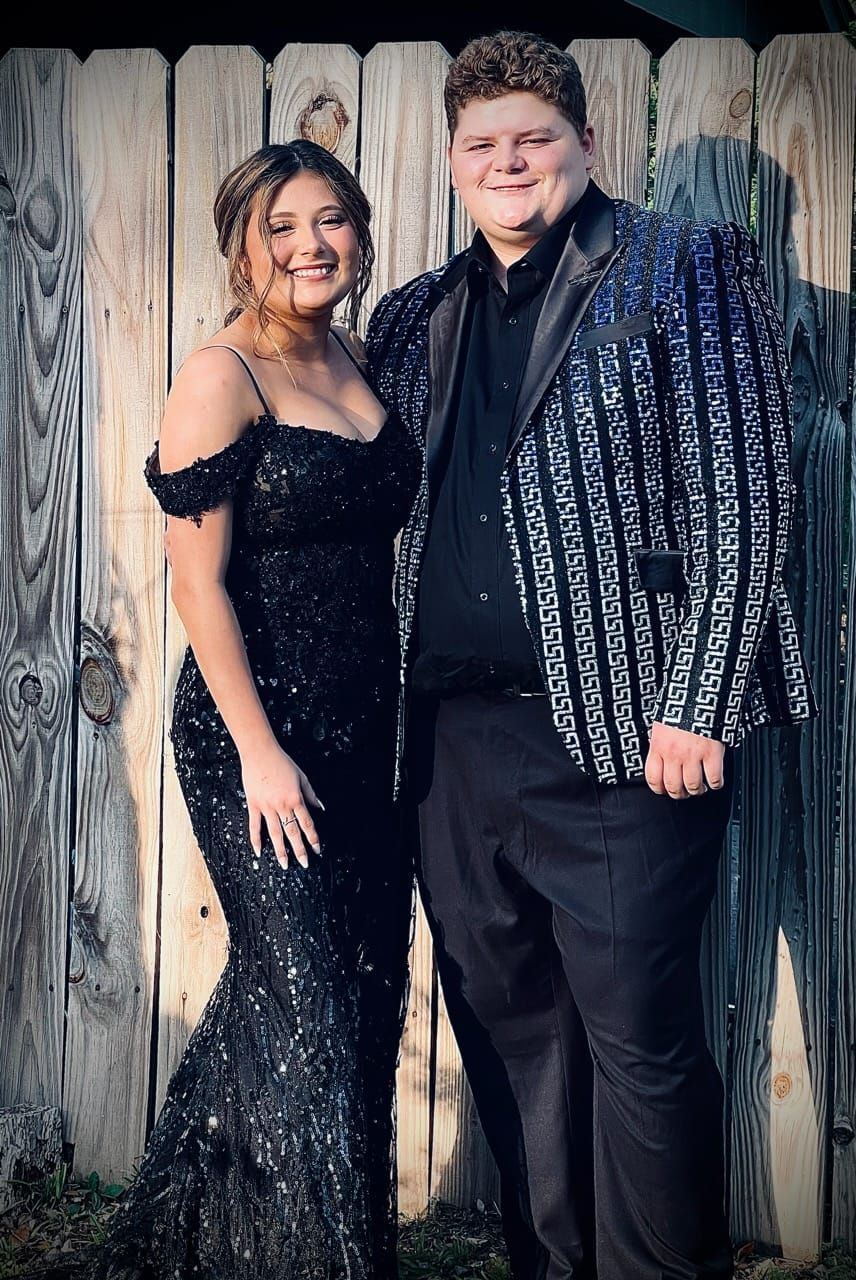 A man and a woman are posing for a picture in front of a wooden fence.