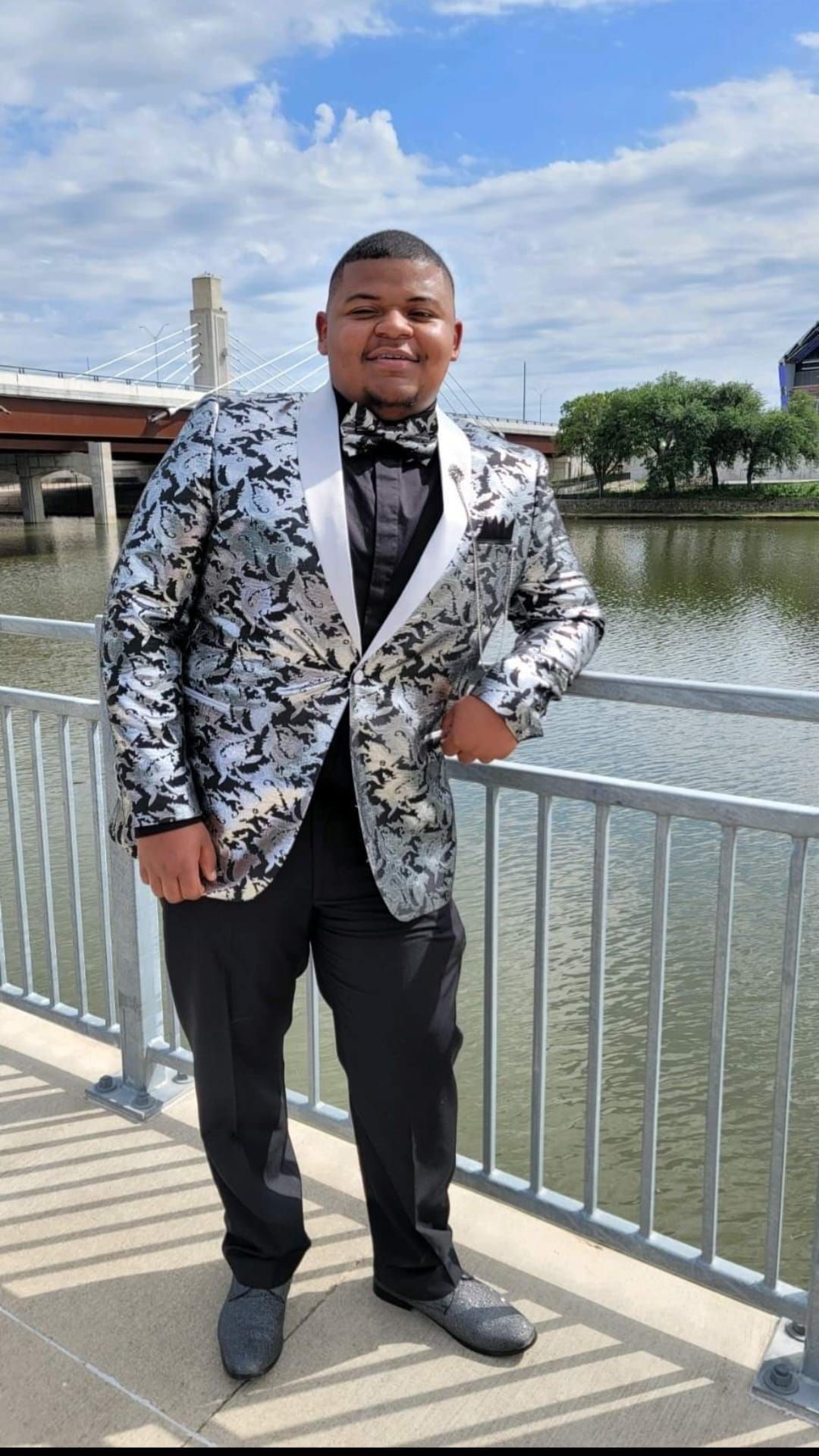 A man in a tuxedo is standing on a bridge next to a body of water.
