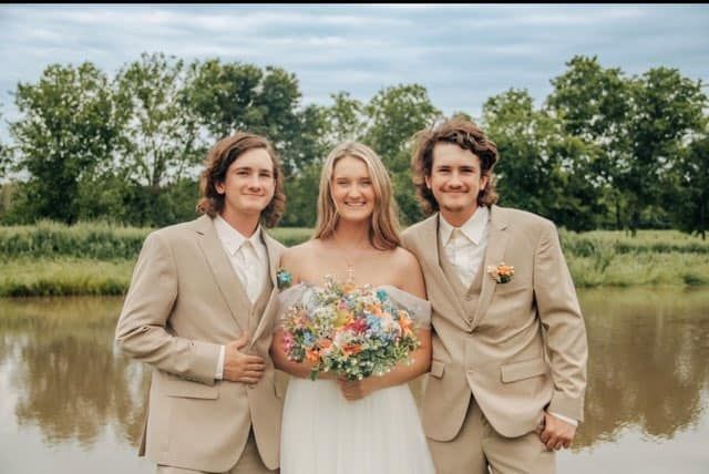 A bride and her two groomsmen are posing for a picture in front of a lake.