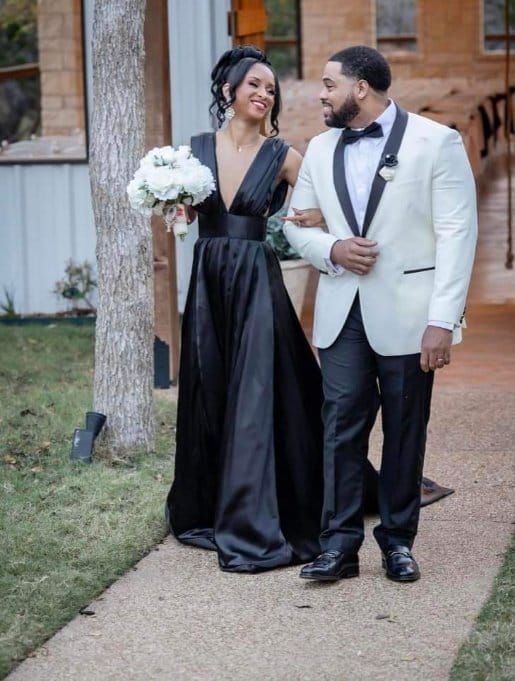 The bride is wearing a black dress and the groom is wearing a white tuxedo.