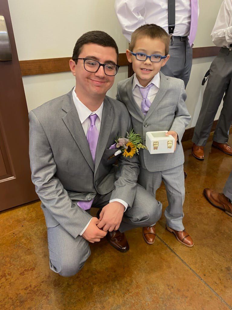 A man in a suit and tie is kneeling next to a boy in a suit and tie.