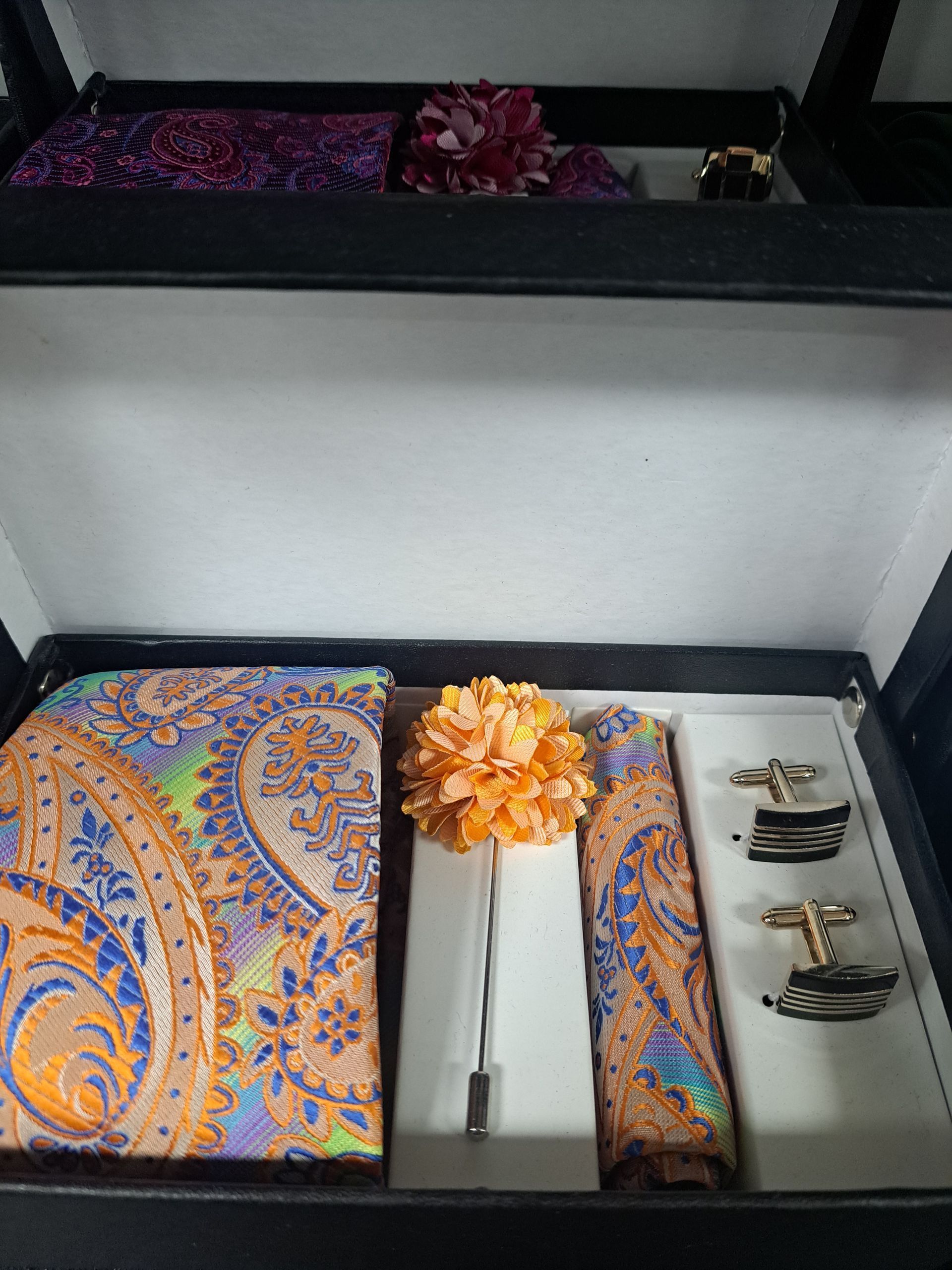 a box filled with a orange and blue paisley pattern tie, pocket square, and cufflinks.