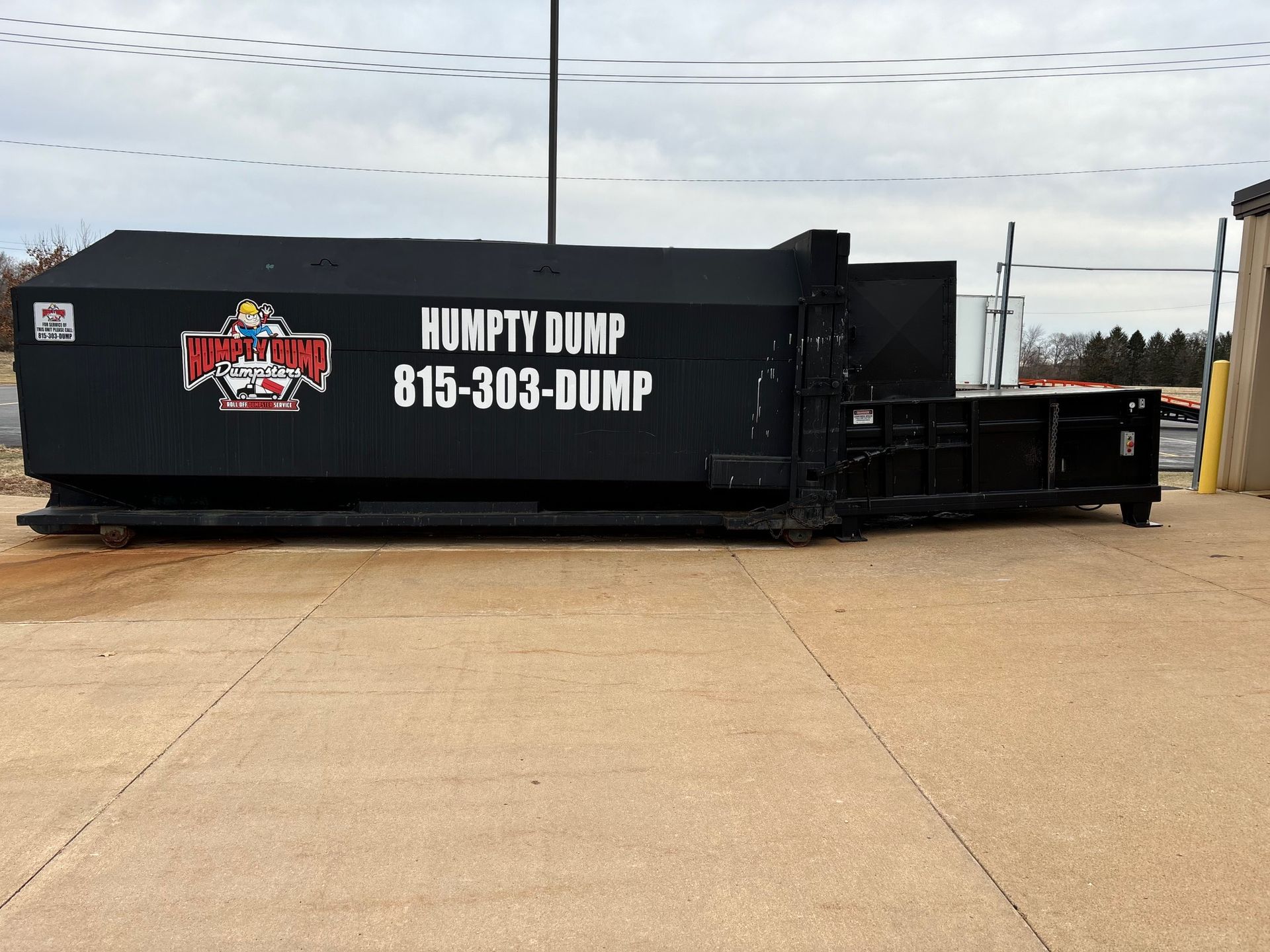 Black Honfifty Dump dumpster with logo and phone number, on a concrete surface.