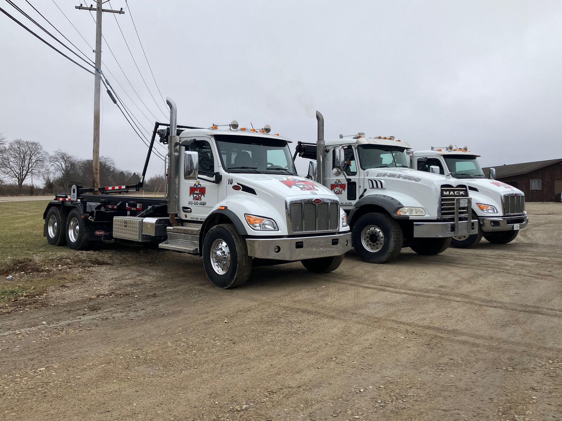 Black dumpster with Humpty Dump logo and phone number, sitting outside on concrete, overcast sky.