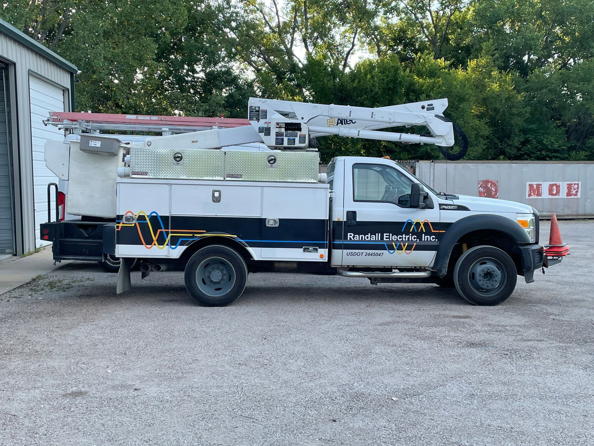 A white truck with a crane on top of it is parked in a gravel lot.