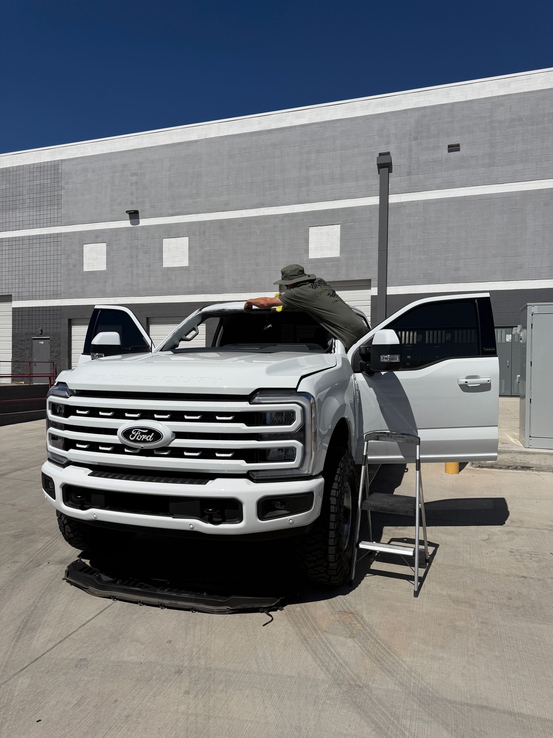 Person working on open hood of white pickup truck in parking lot