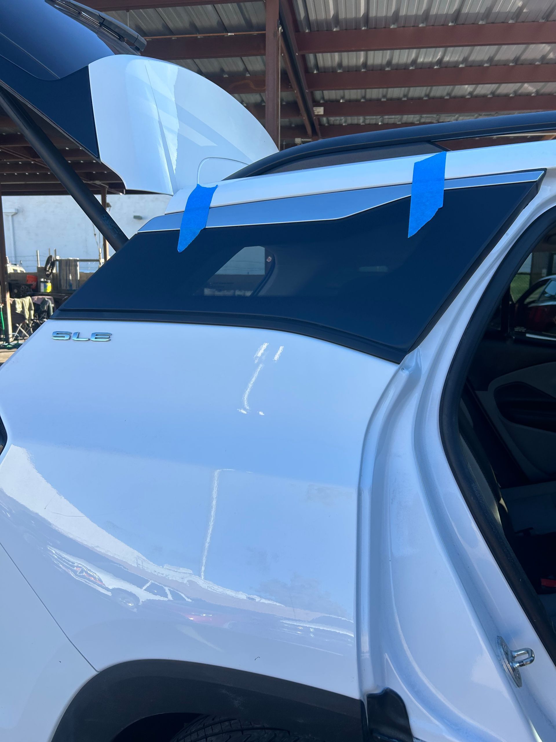 White car with a raised hatchback trunk, blue tape, and a tent-like structure in the background