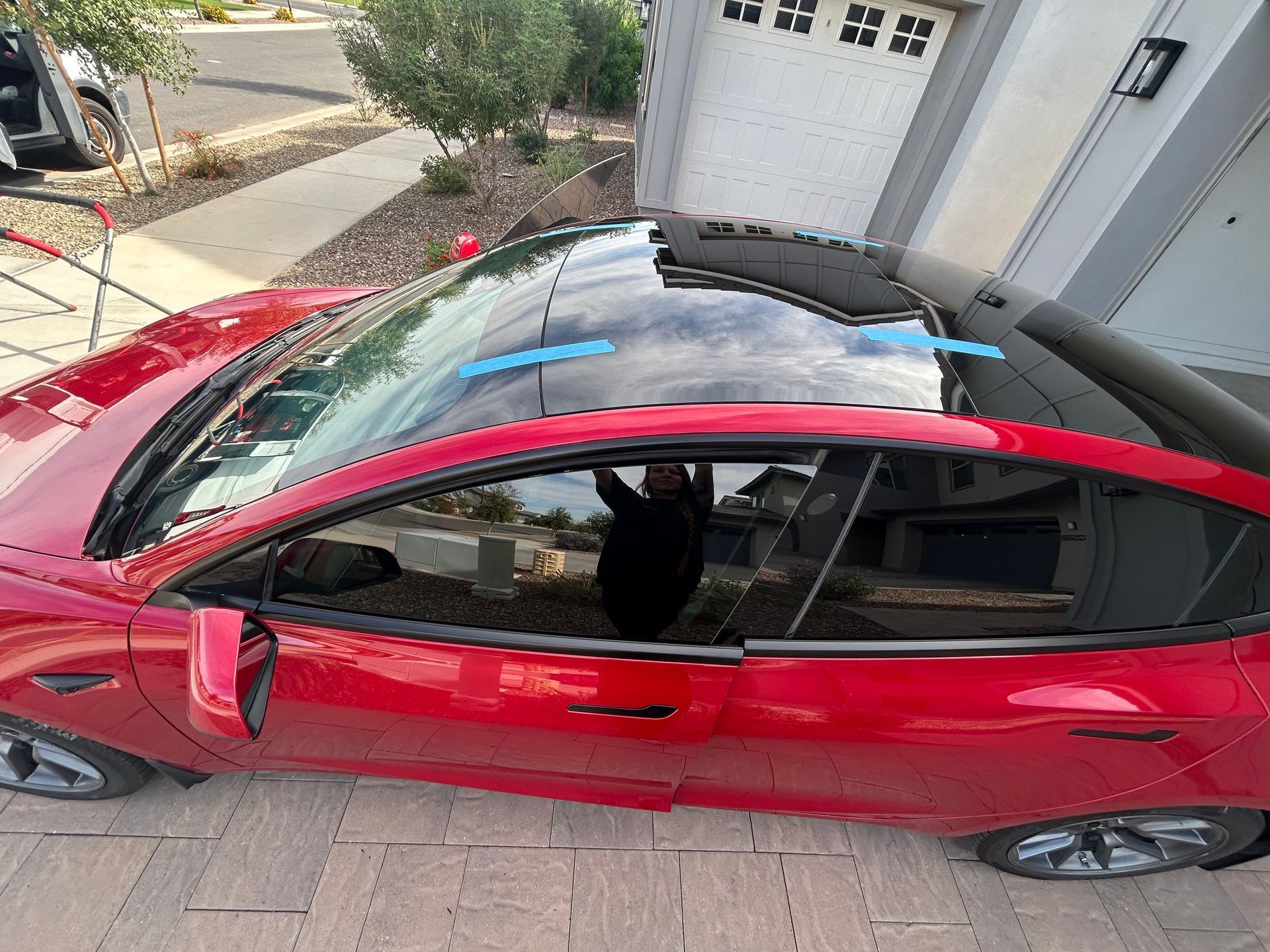 Red car parked in a driveway beside a garage, viewed from above