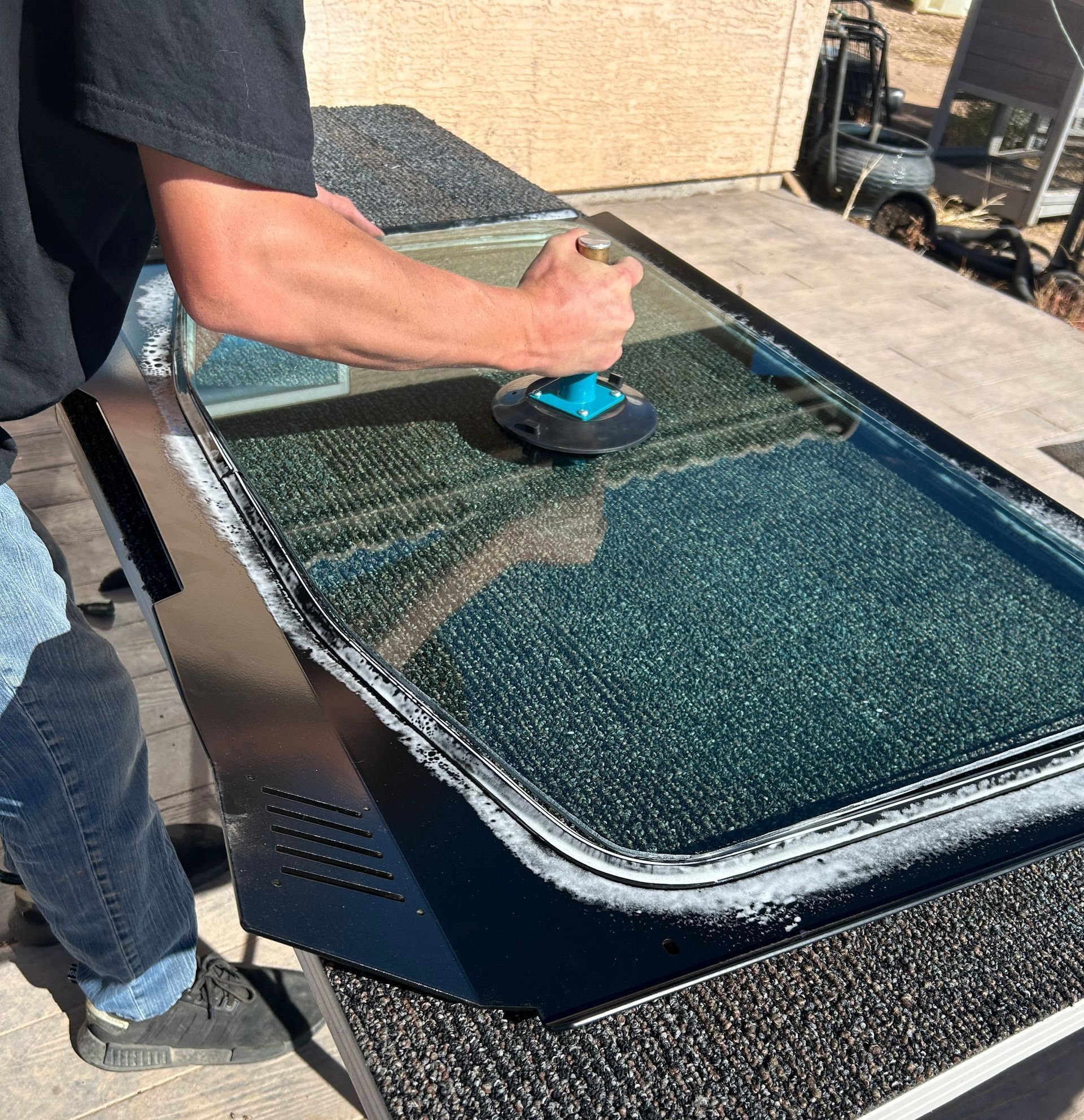 Person polishing a black glass surface with a blue buffer outdoors.