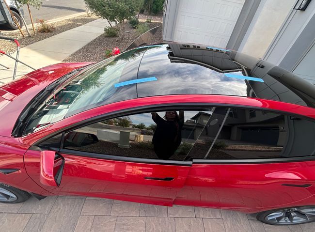 Red sports car with a black roof parked in a driveway, seen from above.