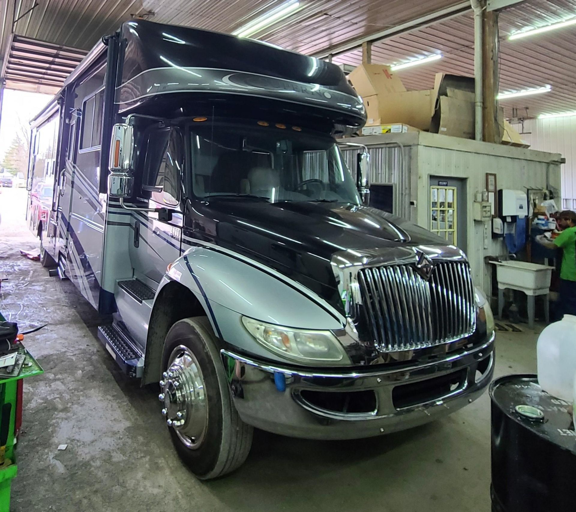 A black and silver International brand truck-based RV parked inside an industrial workshop.