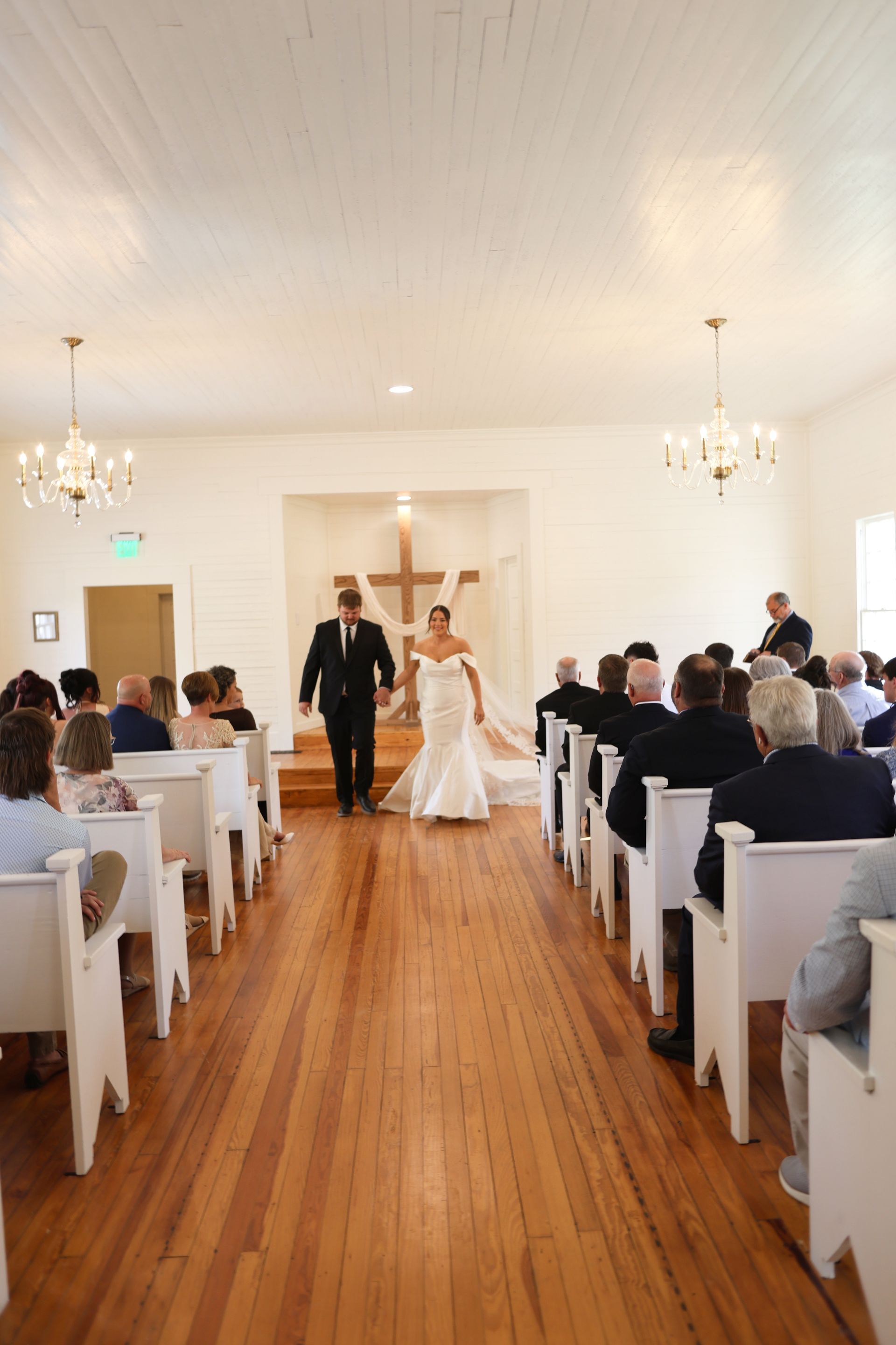 Wedding couple walking down the aisle in a white church, following ceremony.