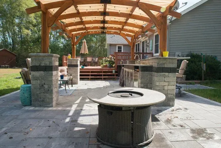 Backyard patio with wooden pergola, outdoor kitchen, and fire pit.