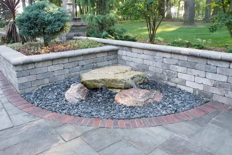 Landscaped garden bed with stone wall and dark gray gravel surrounding large rocks.