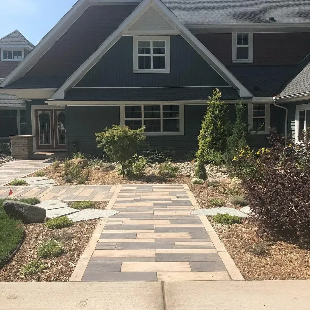 Stone pathway leading to a house with blue siding and brown roof. Landscaping with small plants on either side.