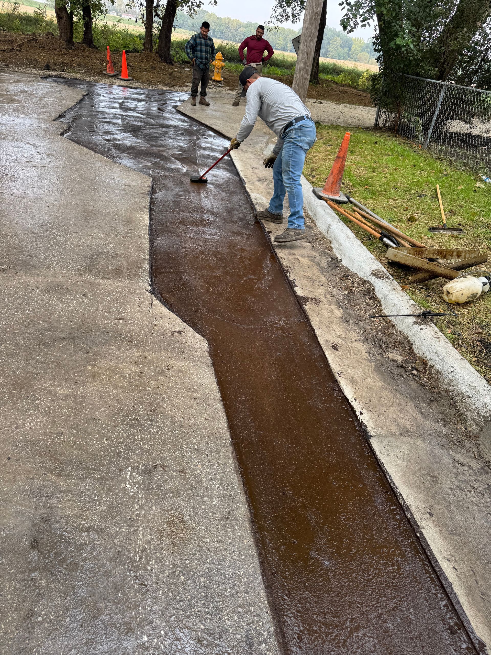 A worker spreads dark sealant onto a long, rectangular trench cut into a concrete surface, with two observers nearby.