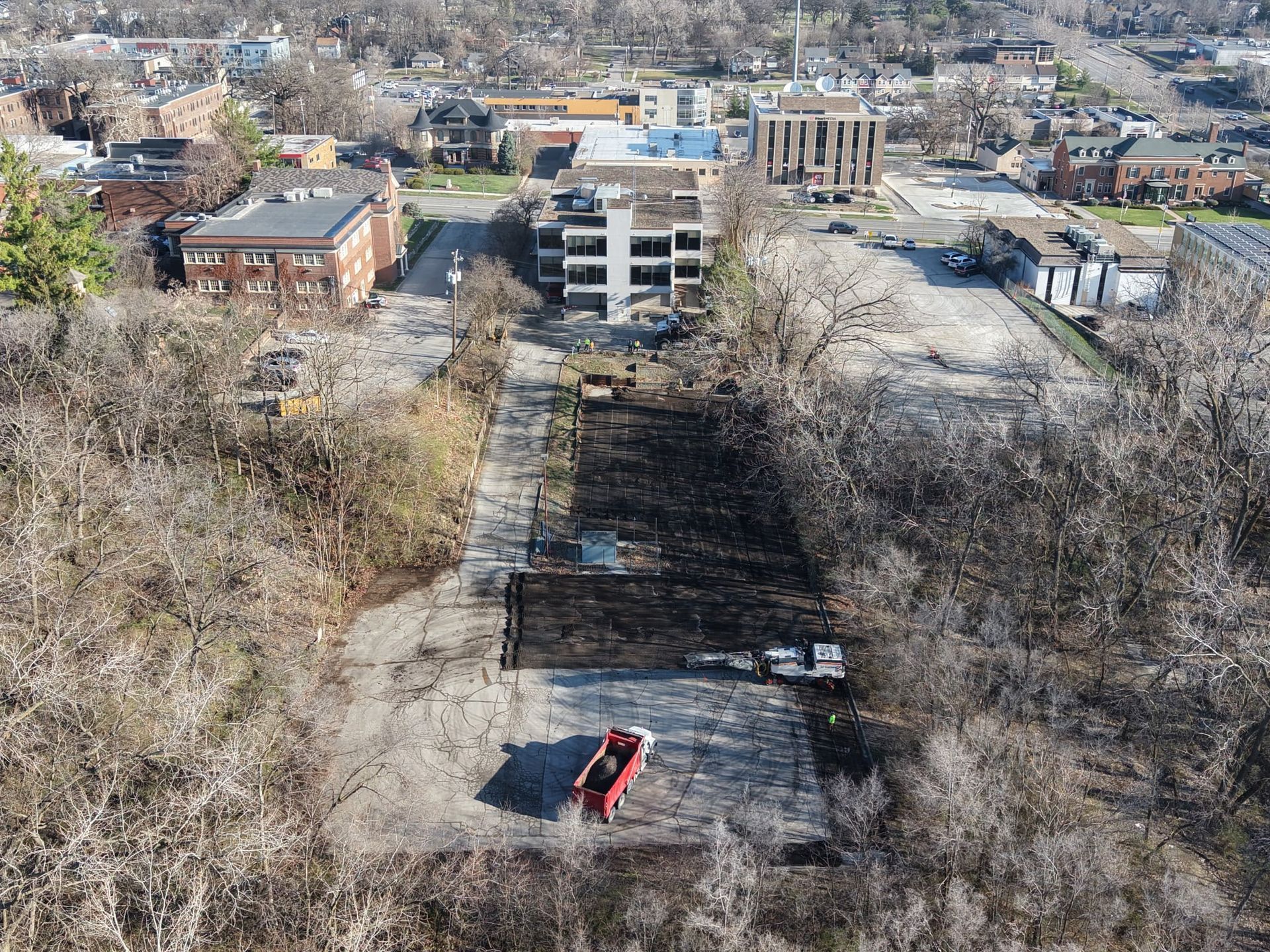 Aerial view of a cleared dirt lot with a red truck, next to buildings and trees in a town setting.