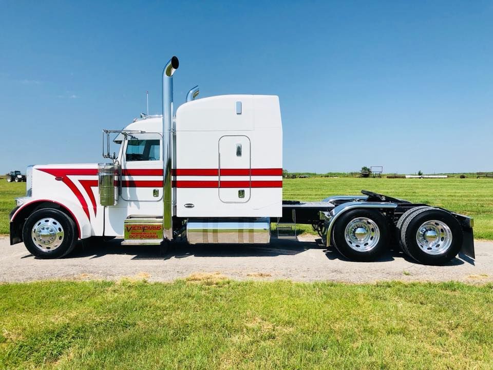 A white semi truck with a red stripe on the side is parked in a grassy field.