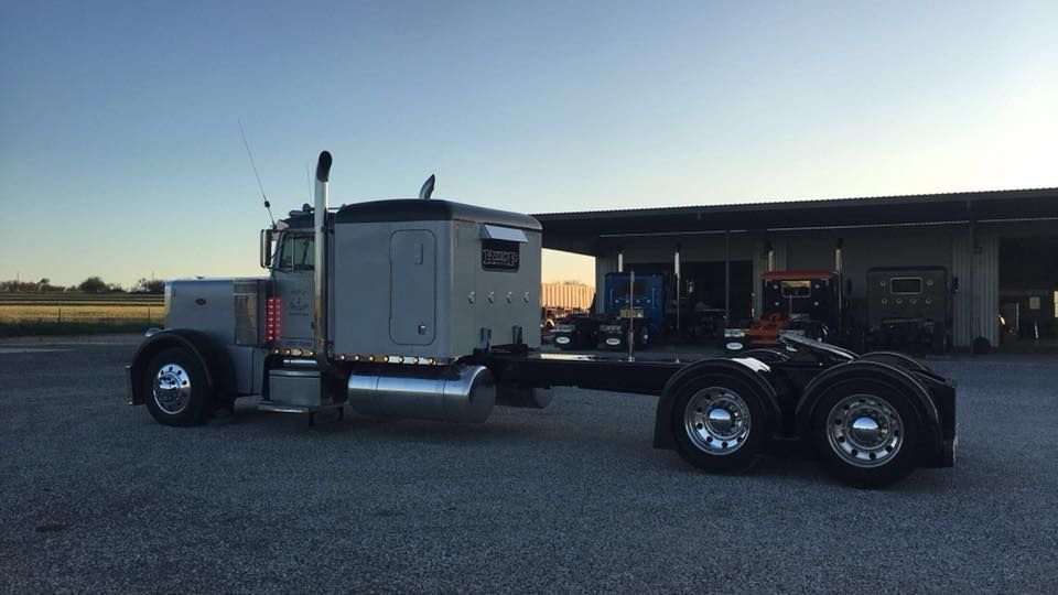 A semi truck is parked in a gravel lot in front of a building.