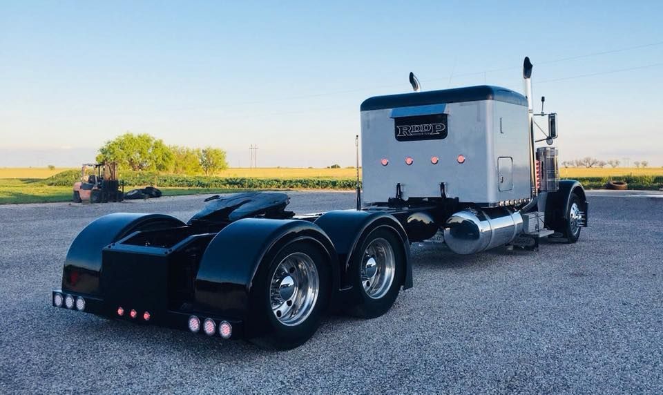 A semi truck with a trailer attached to it is parked in a gravel lot.
