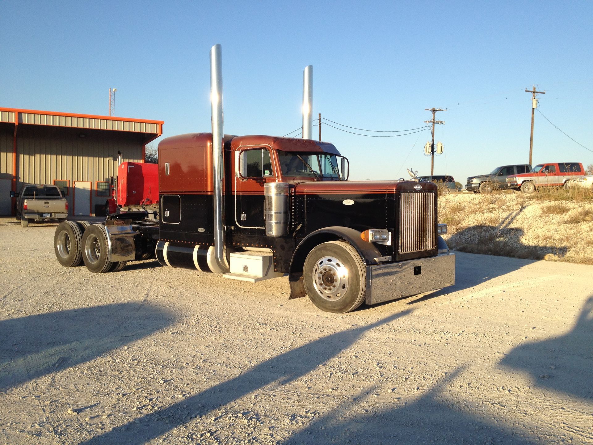A red and black semi truck is parked in a gravel lot