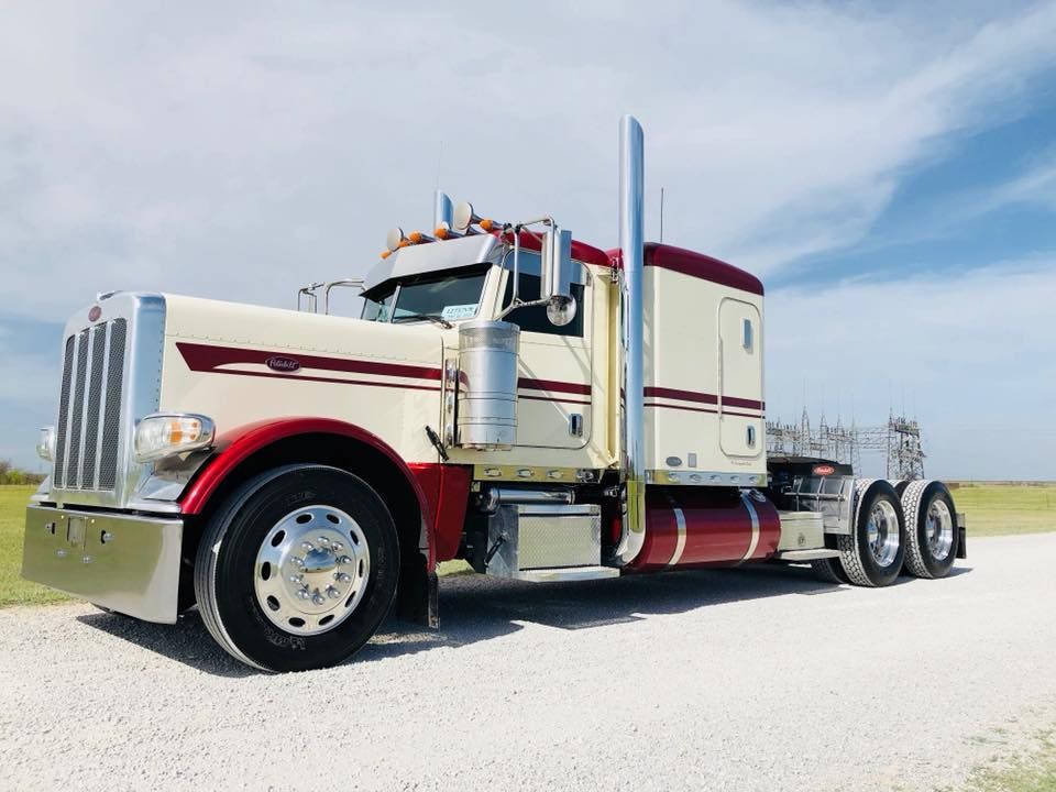 A red and white semi truck is parked on a gravel road.