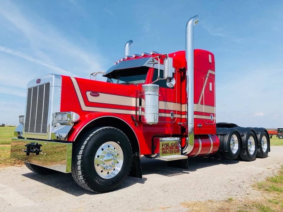 A red semi truck is parked on a dirt road.