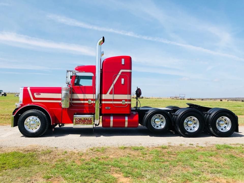 A red semi truck is parked in a grassy field.