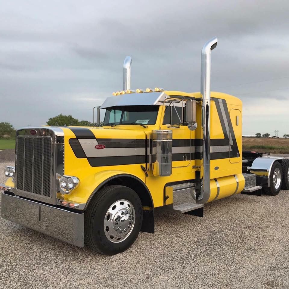 A yellow semi truck is parked in a gravel lot