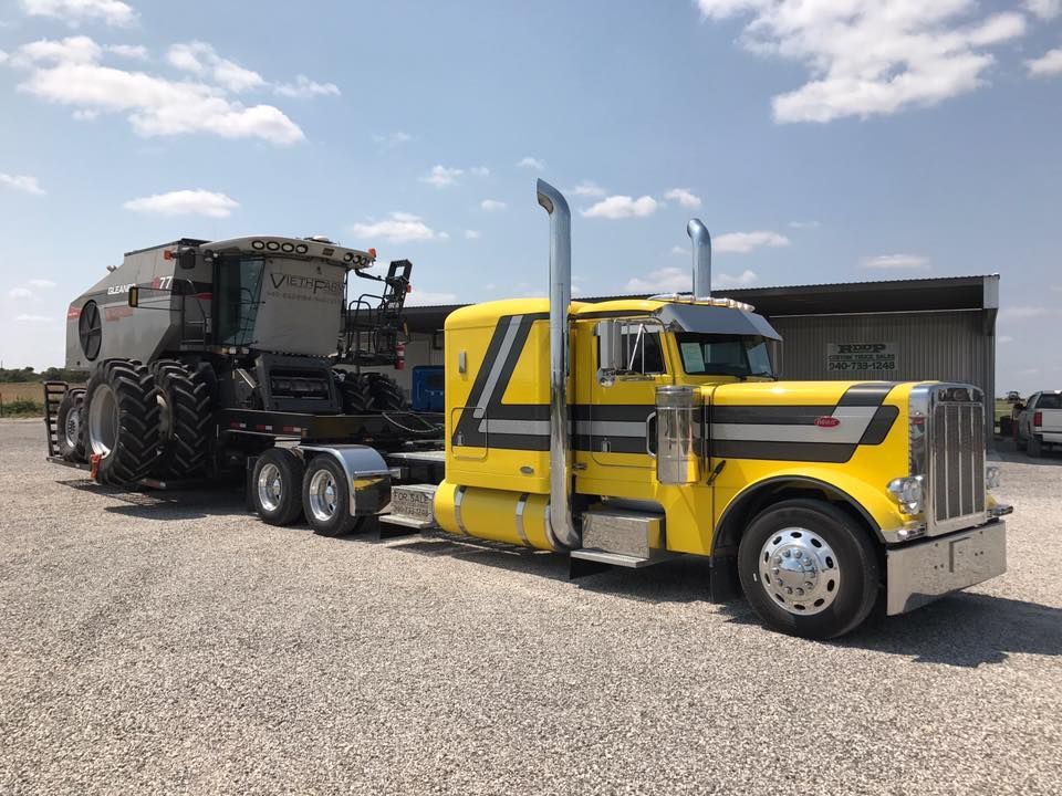 A yellow semi truck is towing a tractor in a gravel lot.
