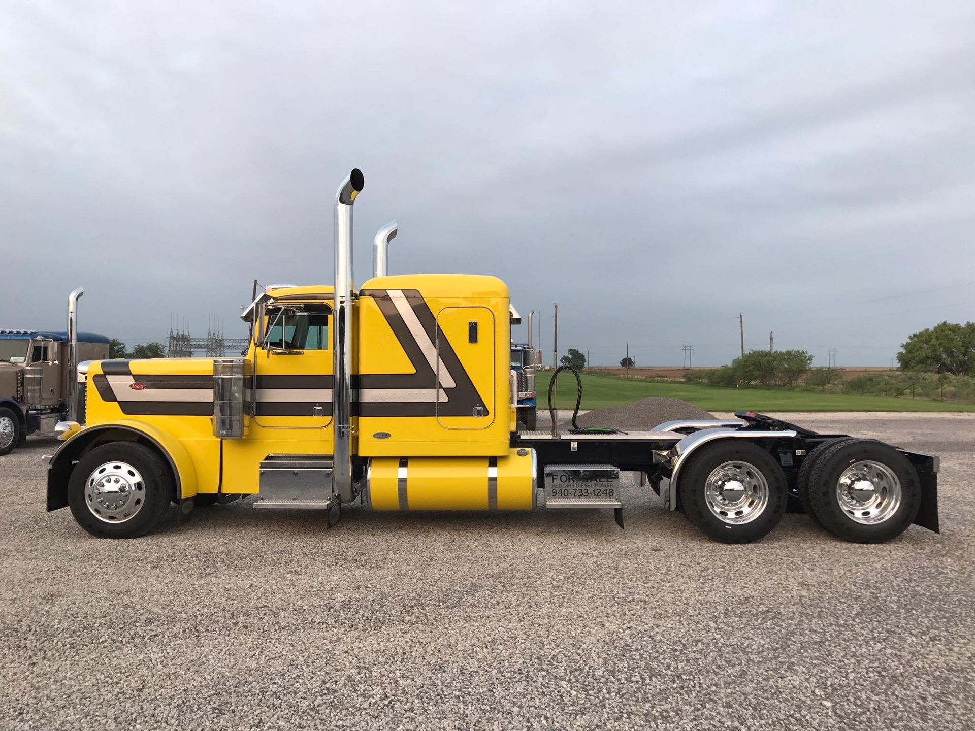 A yellow semi truck is parked in a gravel lot.