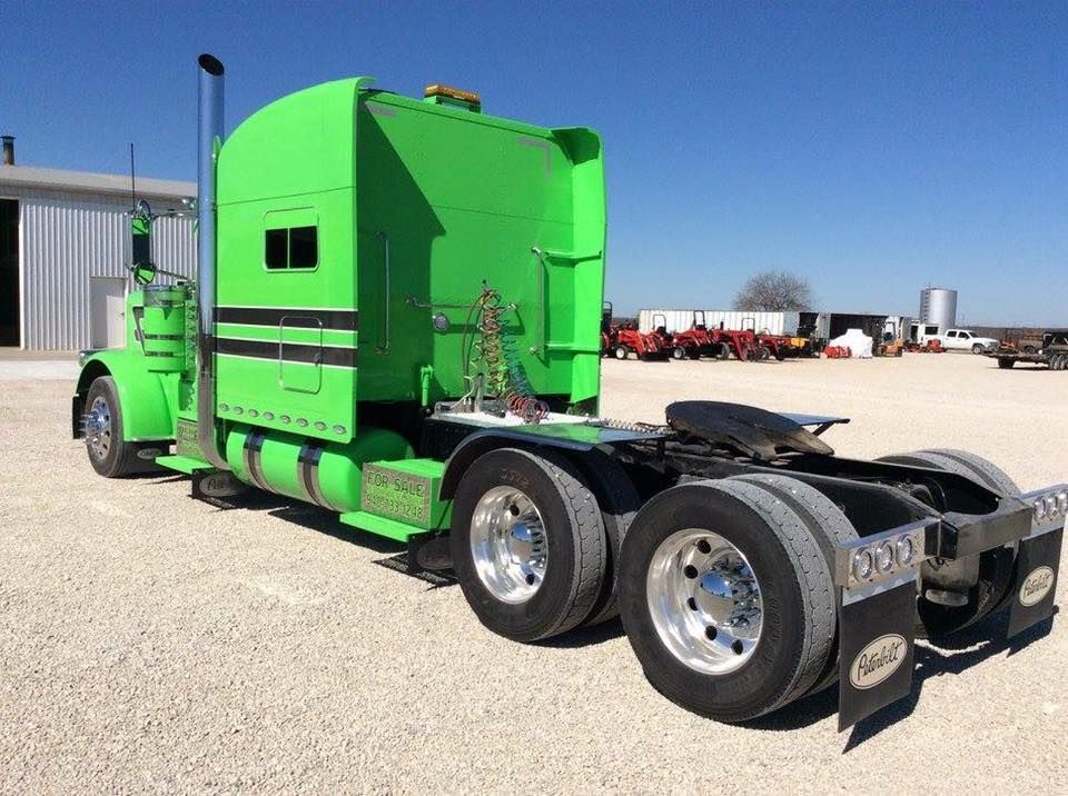 A green semi truck is parked in a gravel lot