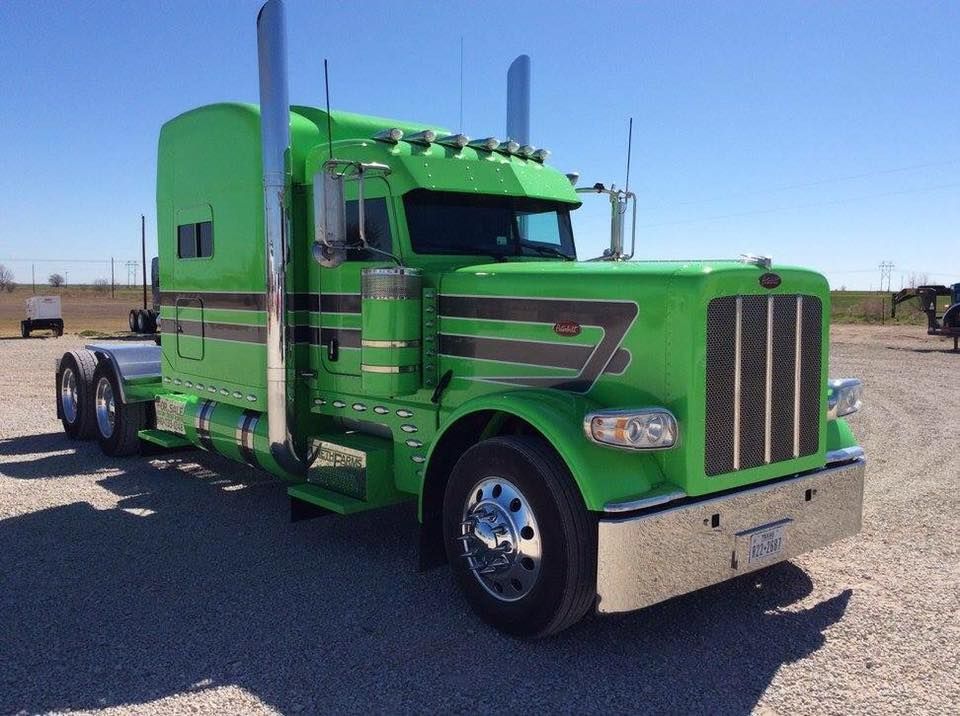 A green semi truck is parked in a gravel lot.