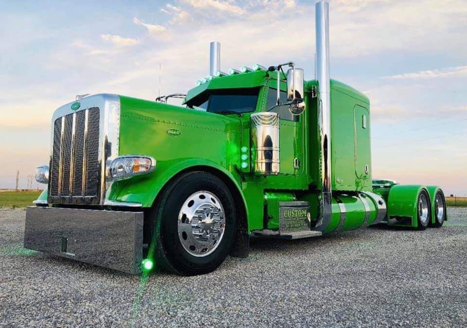 A green semi truck is parked on a gravel road.
