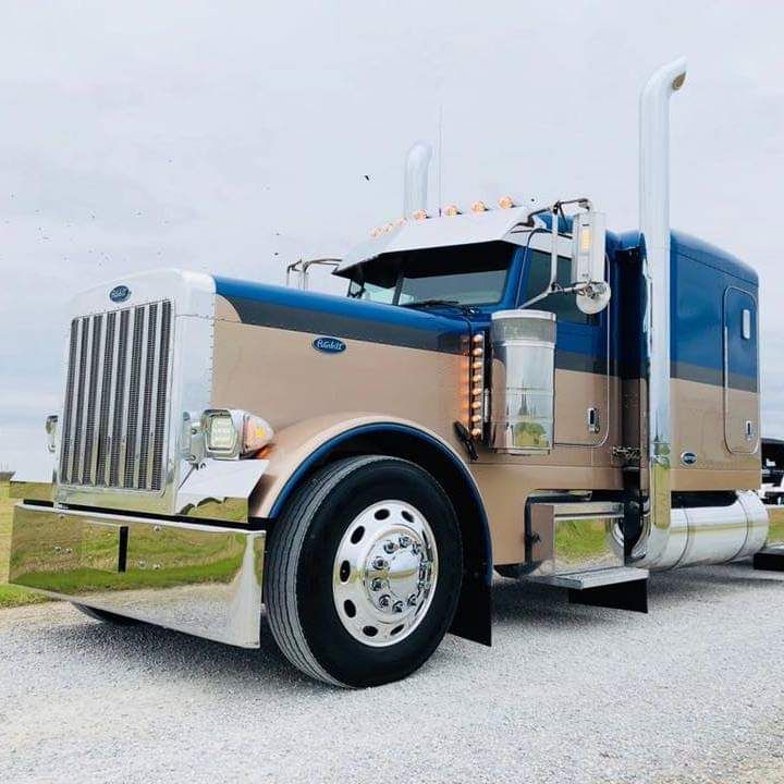 A blue and tan semi truck is parked on a gravel road