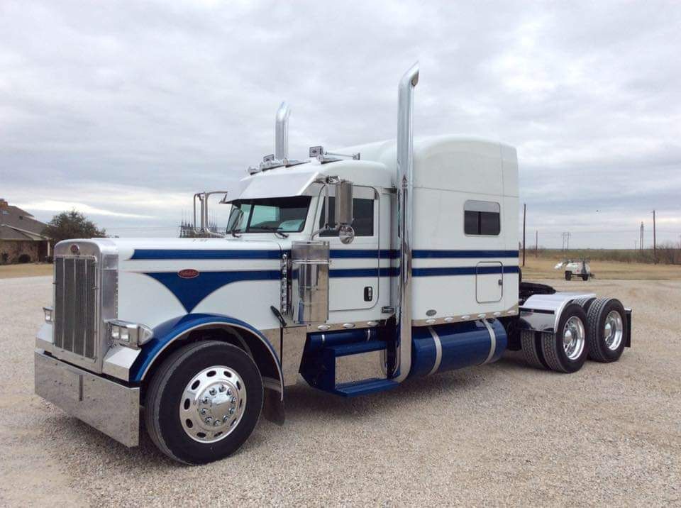 A white and blue semi truck is parked in a gravel lot.