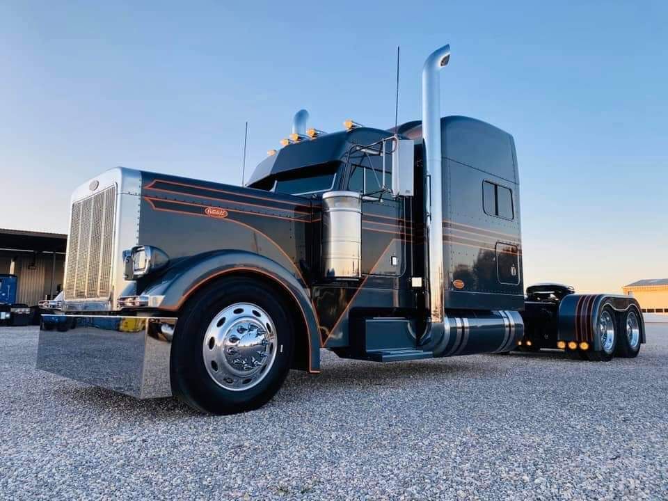 A black semi truck is parked in a gravel lot.