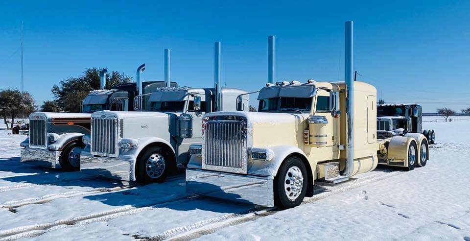 A row of semi trucks are parked in the snow.