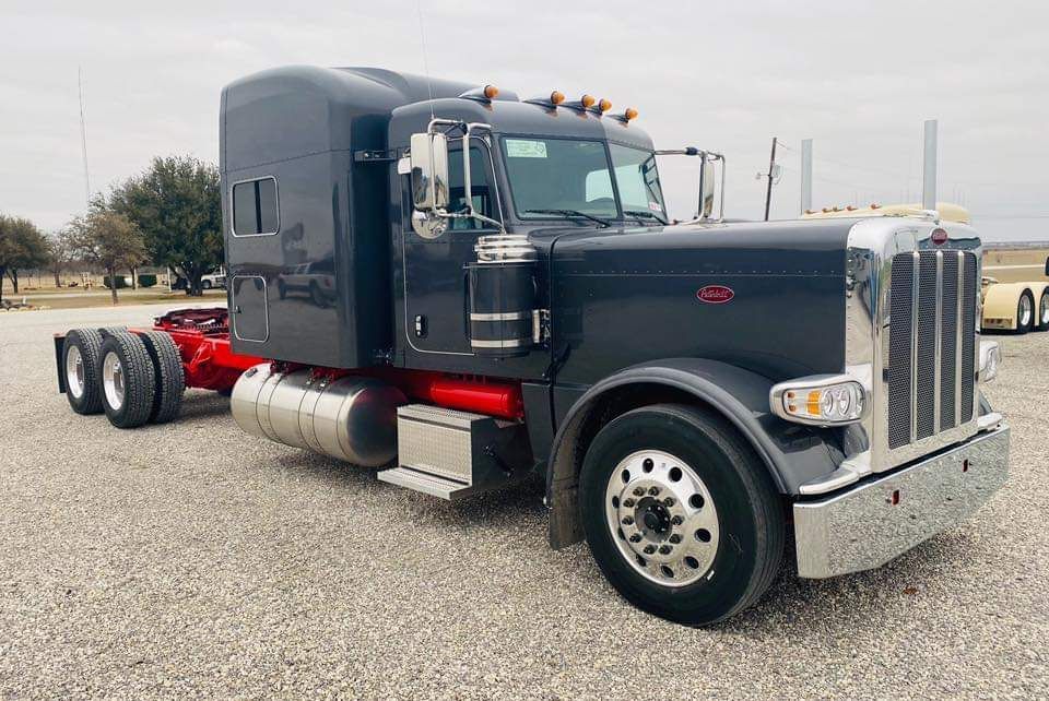 A black semi truck is parked in a gravel lot.