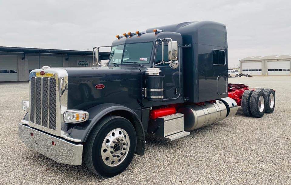 A black semi truck is parked in a gravel lot.