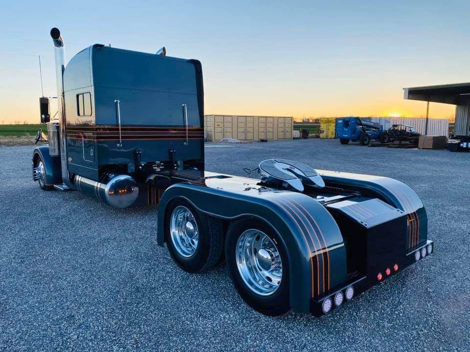 A black semi truck is parked in a gravel lot.