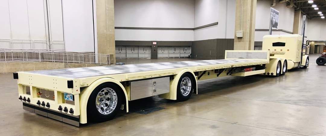 A semi truck with a flatbed trailer is parked in a warehouse.
