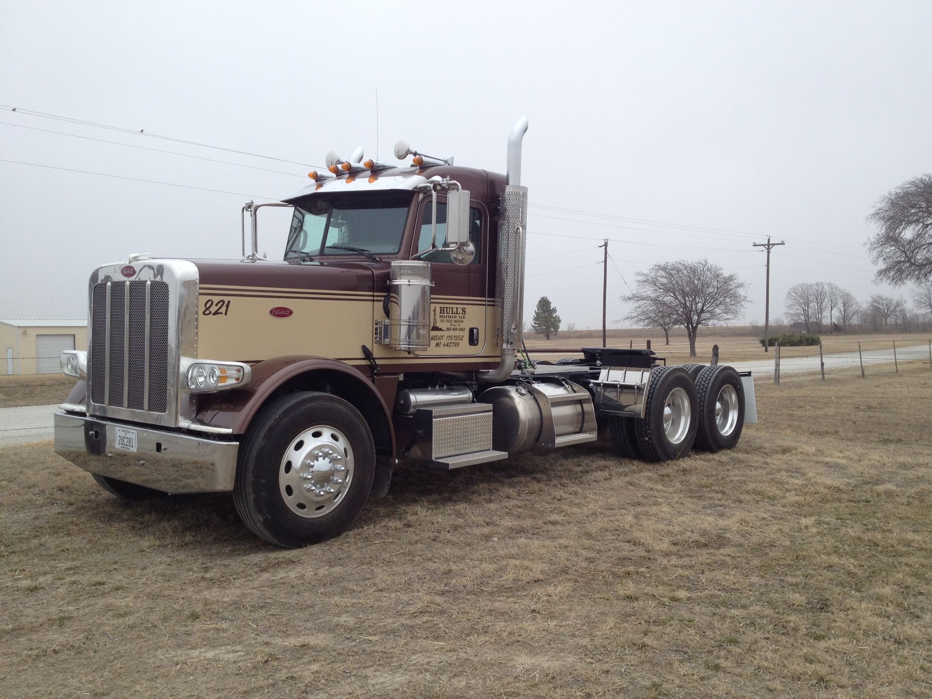 A brown and silver semi truck is parked in a field.
