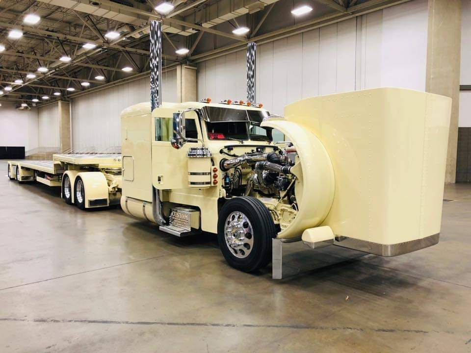 A yellow semi truck with the hood open is parked in a warehouse.