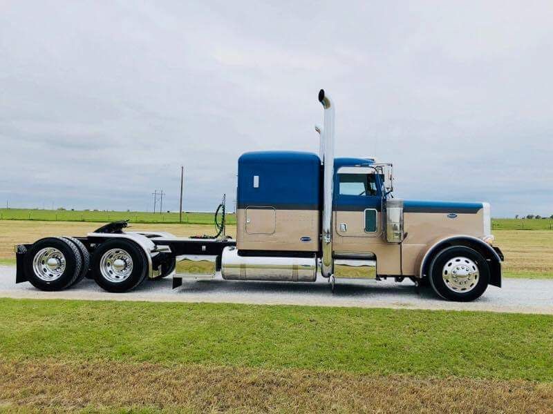 A blue and tan semi truck is parked in a grassy field.