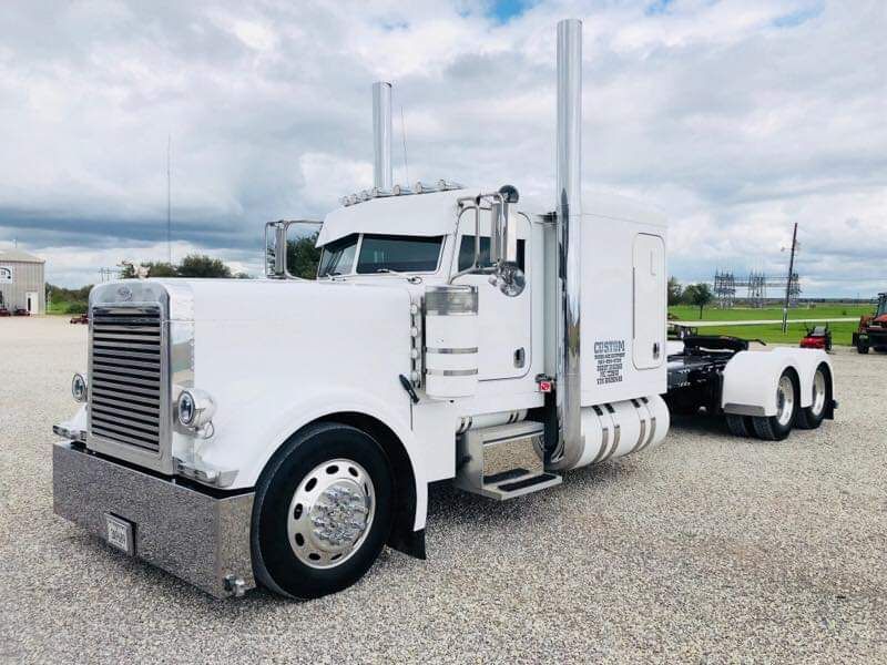 A white semi truck is parked in a gravel lot.